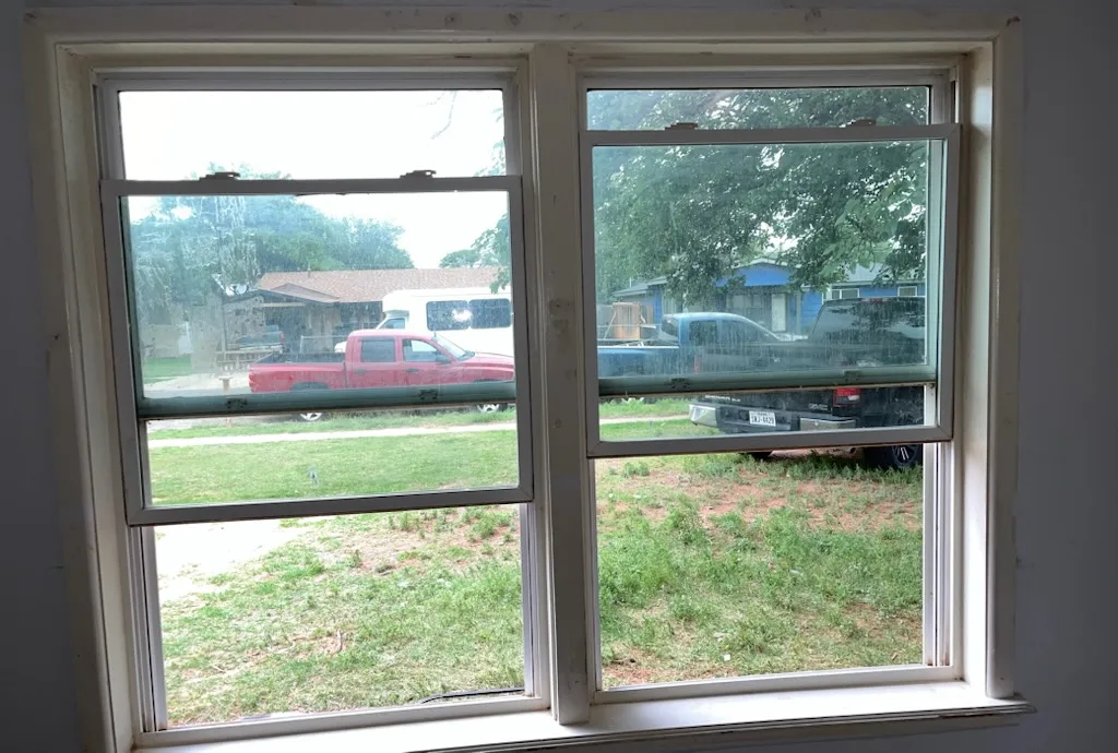Window seen from inside before painting, with worn trim, a marked sill and dull gray walls